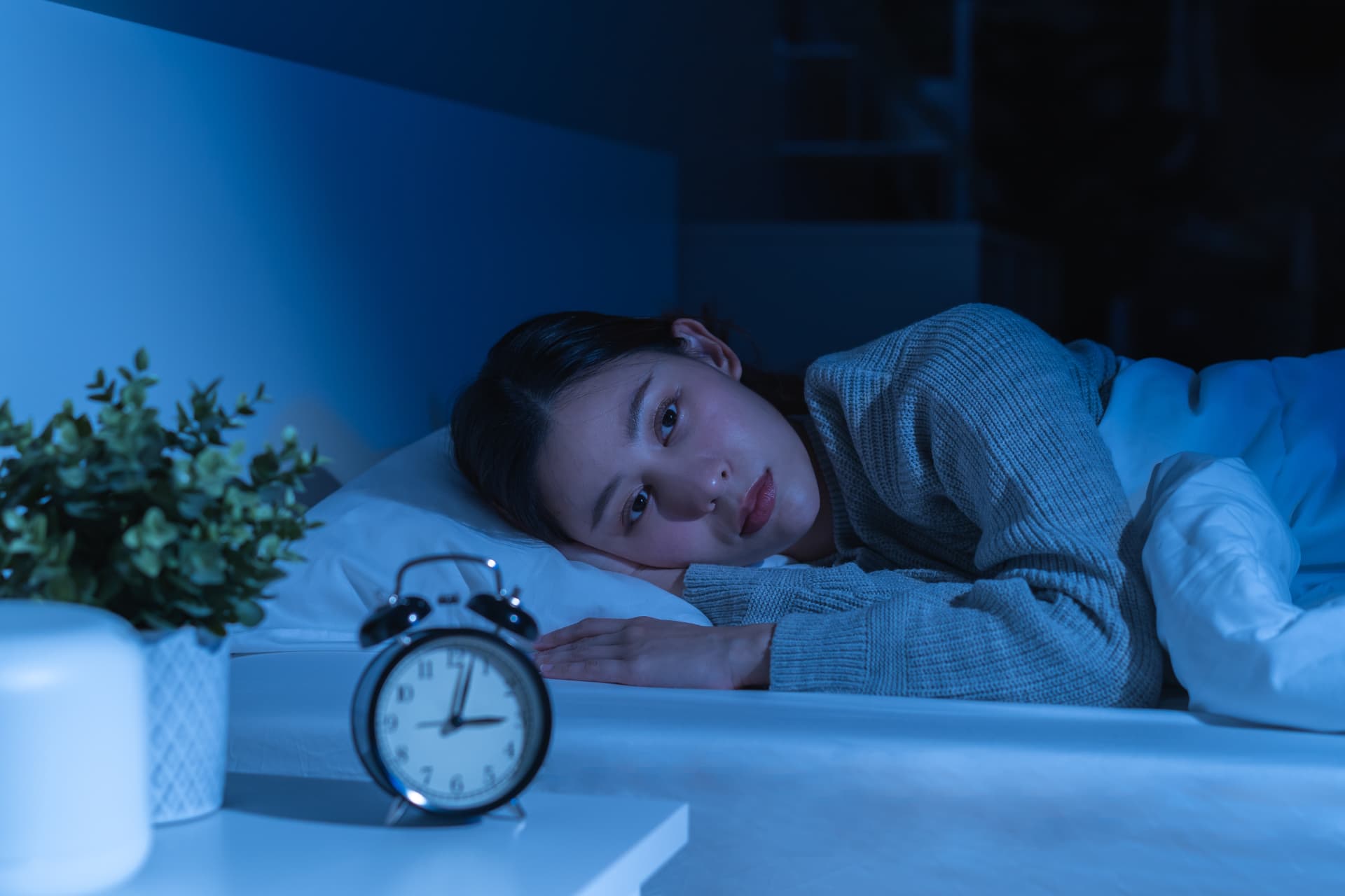 Woman lying awake in bed at night beside an alarm clock